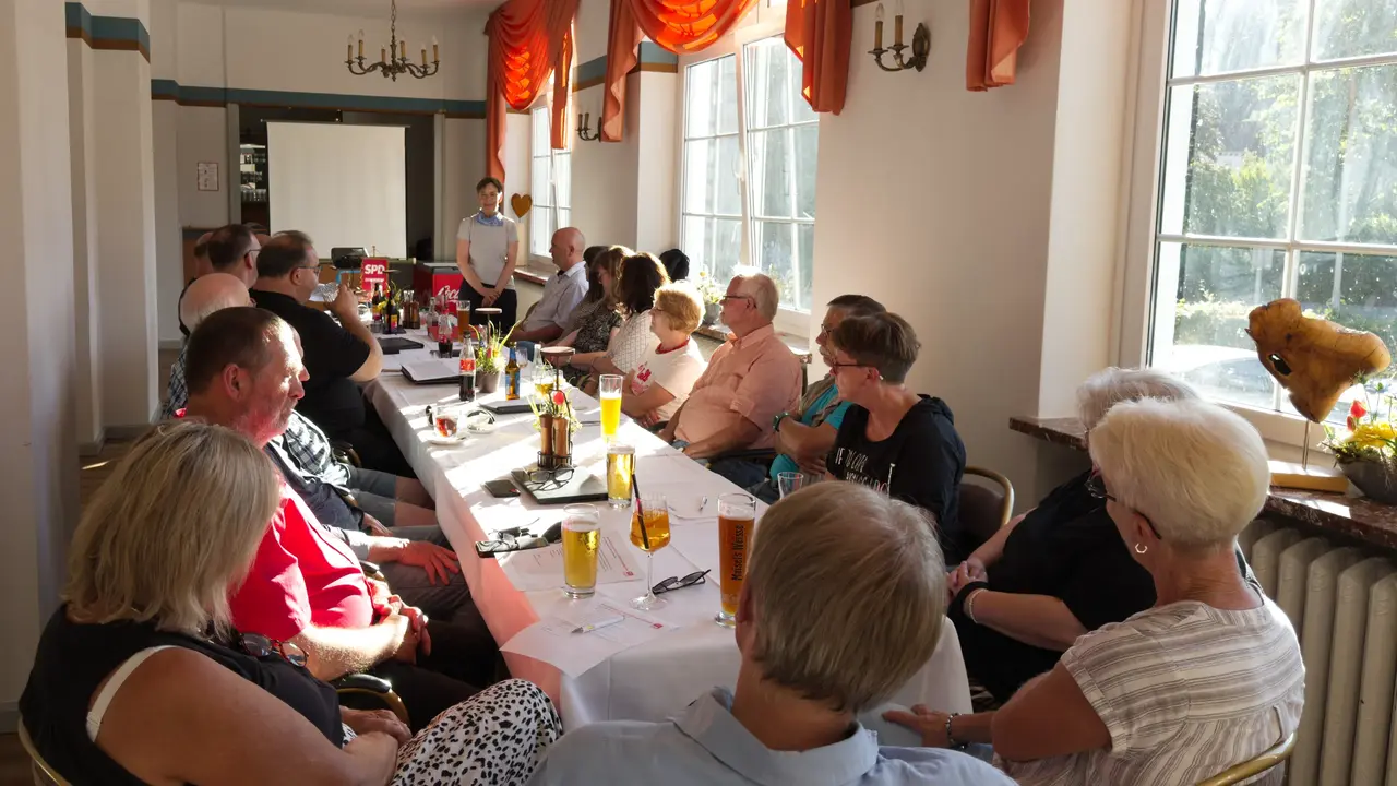 Landratskandidatin Dr. Ulrike Witt spricht stehend vor einer versammelten SPD-Versammlung  an einer langen Tafel in einem hellen Saal.