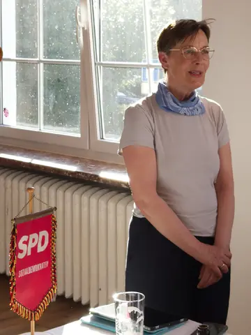 Eine Frau spricht energisch vor einem Fenster. Links neben ihr befindet sich ein SPD-Wimpel.