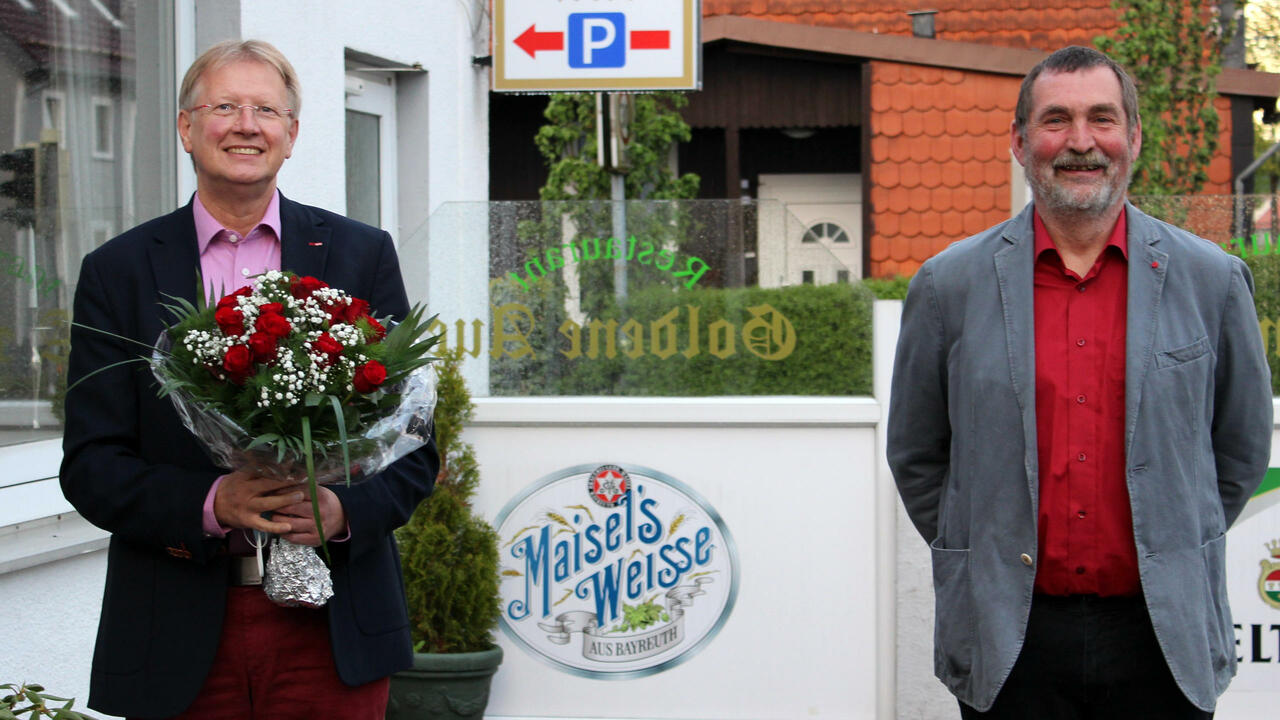 Dr. Thomas Gans und Uwe Speit stehen vor der Goldenen Aue. Thomas Gans hält einen Blumenstrauß.